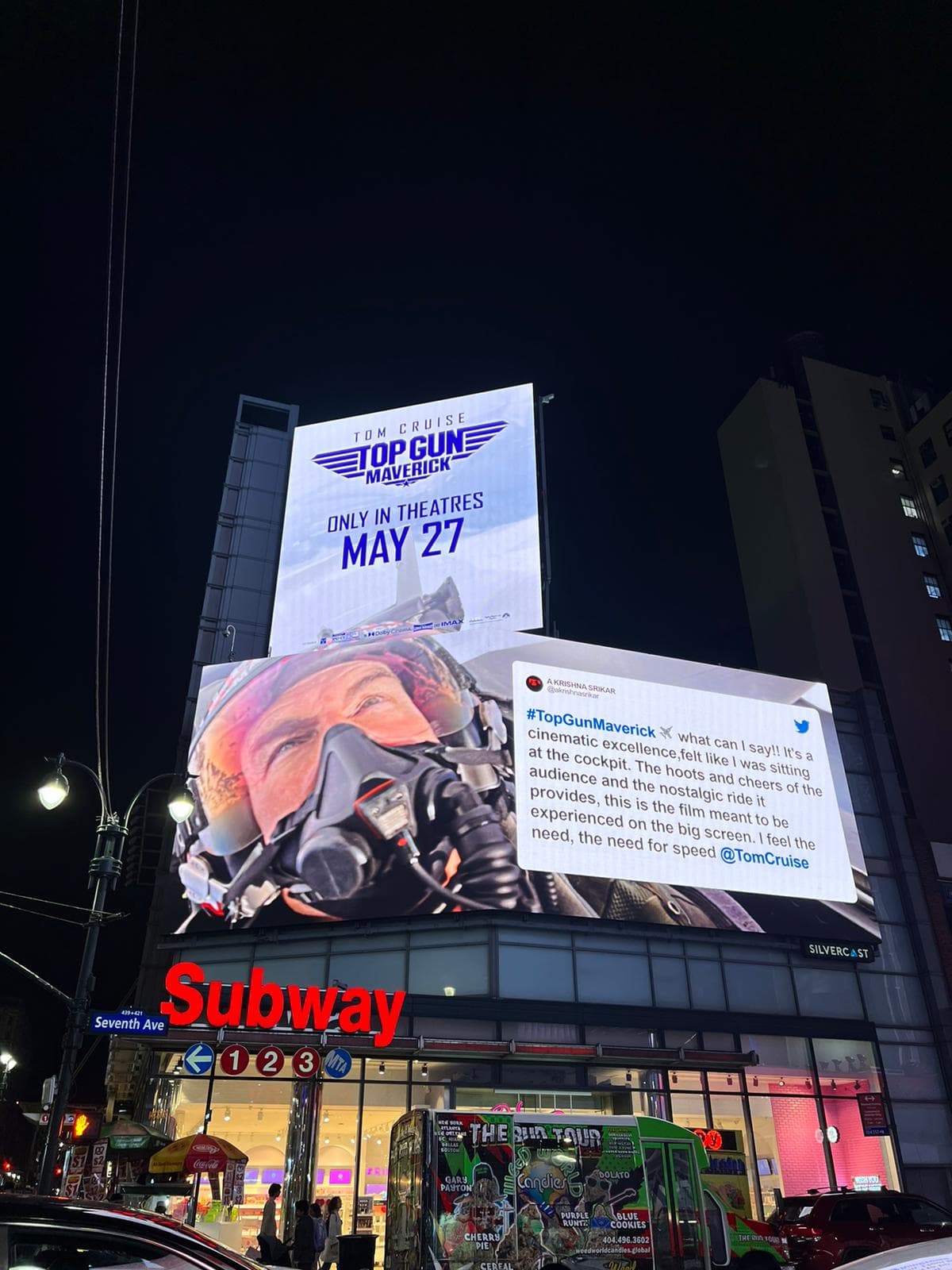 A Times Square billboard at night showing Krishna's Top Gun: Maverick review beside the film's poster, above the Subway on Seventh Avenue